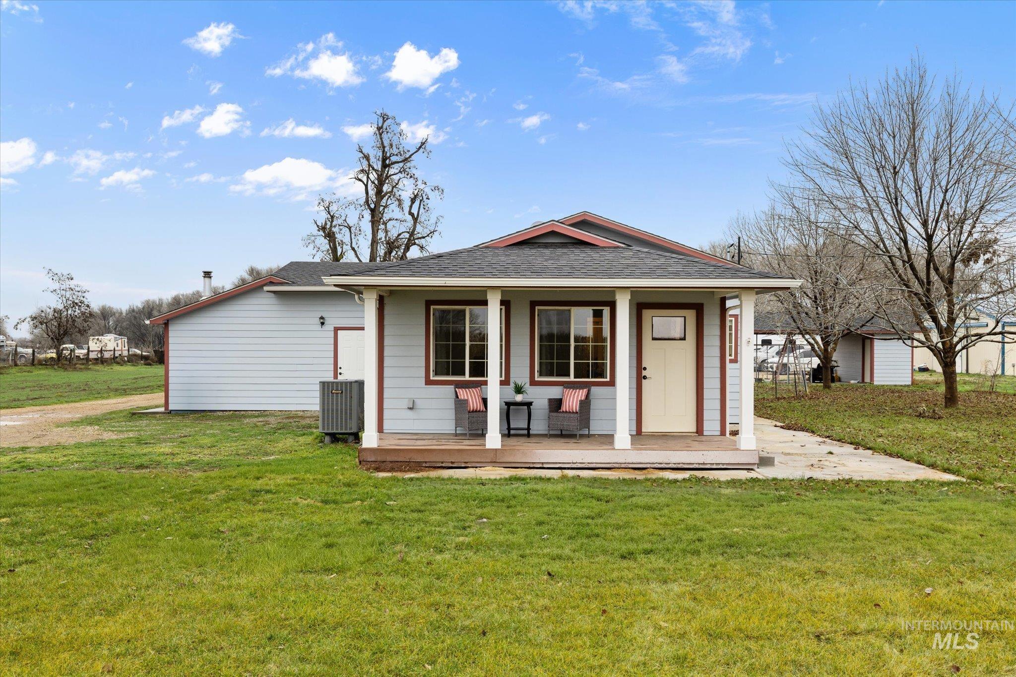 View of front facade featuring a front yard, a porch, roof with shingles, and an outdoor structure