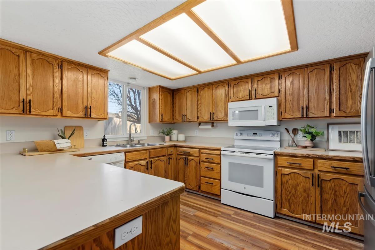 Kitchen featuring brown cabinetry, white appliances, light countertops, and light wood-style flooring