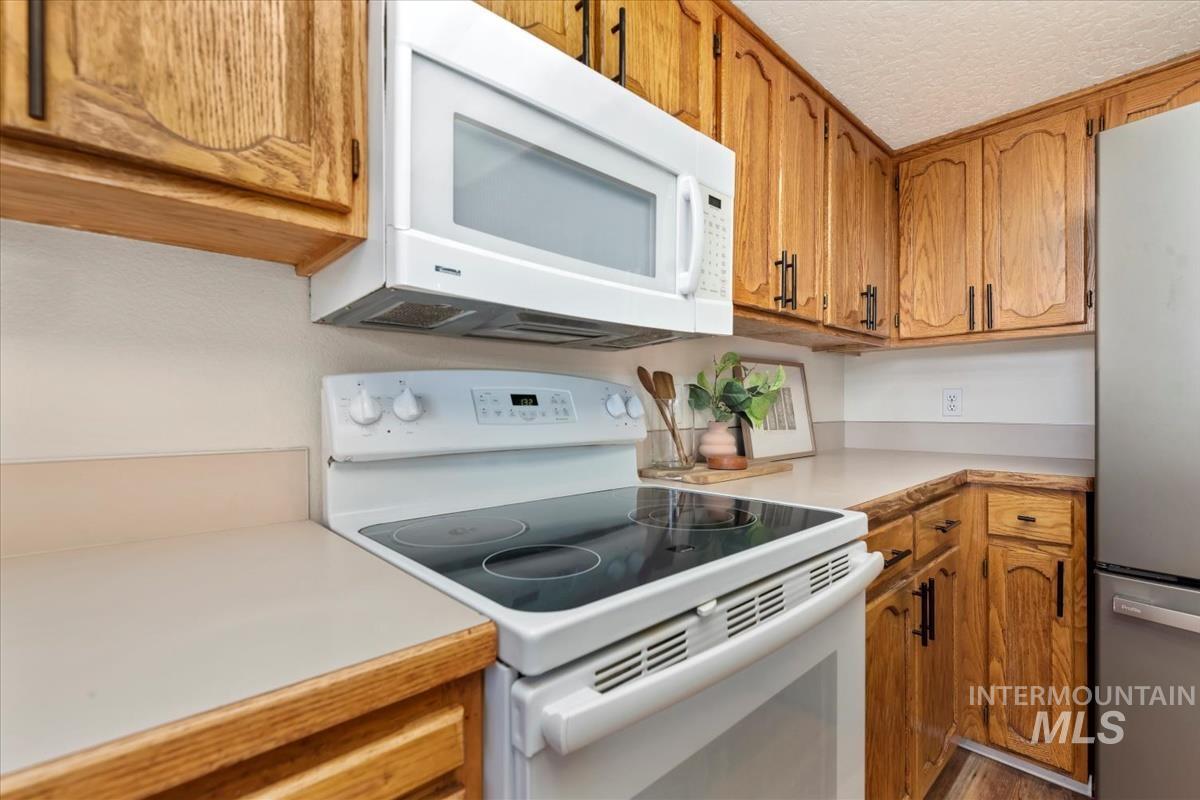 Kitchen featuring white appliances, light countertops, brown cabinetry, and a textured ceiling