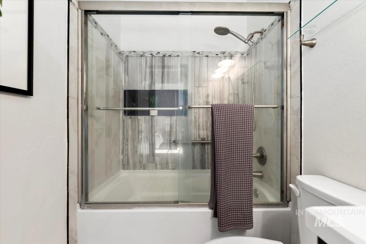 Bathroom featuring bath / shower combo with glass door and a textured wall