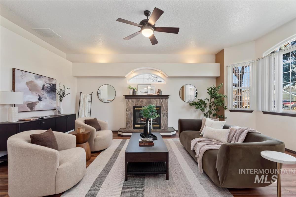 Living area with a high end fireplace, ceiling fan, a textured ceiling, and wood finished floors