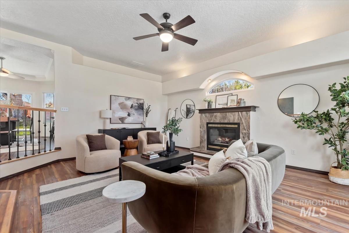 Living room featuring ceiling fan, wood finished floors, a fireplace, and a textured ceiling