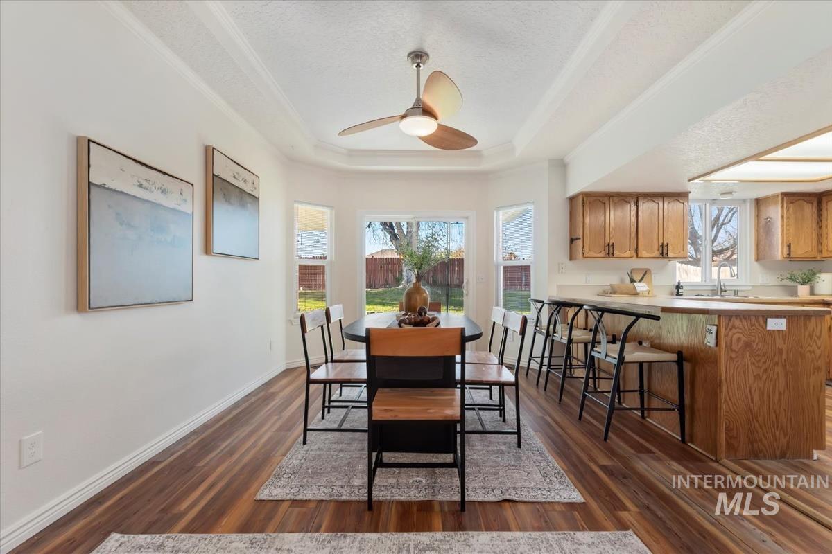 Dining area featuring dark wood-style floors, ceiling fan, a raised ceiling, plenty of natural light, and a textured ceiling
