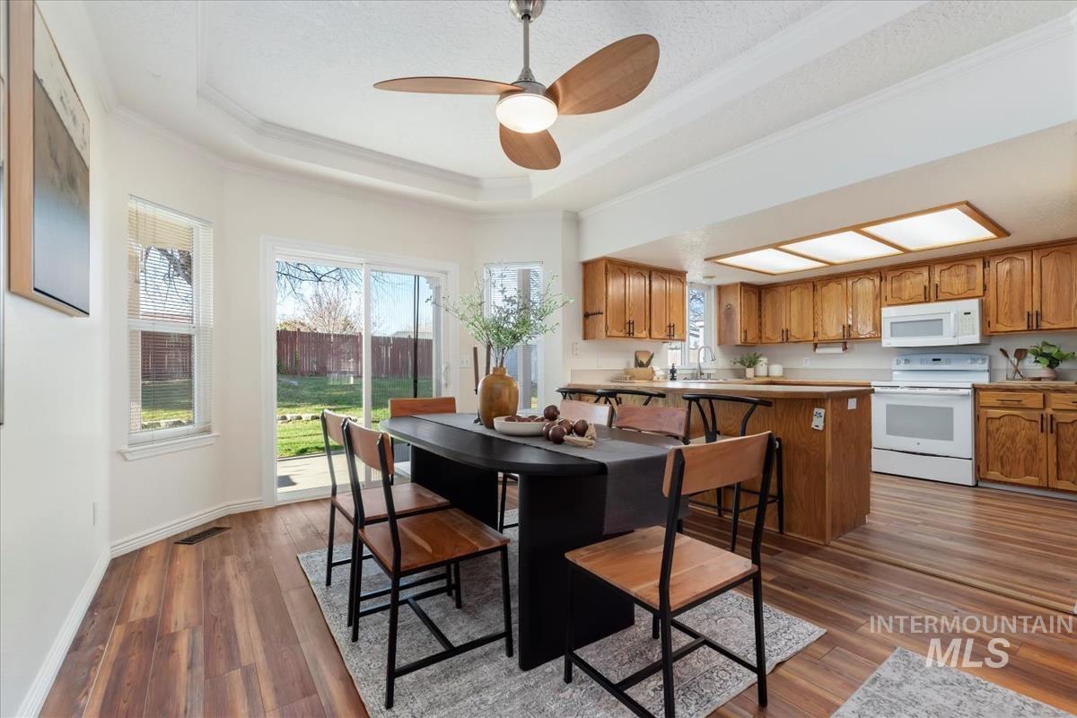Dining space with ornamental molding, a tray ceiling, ceiling fan, and dark wood-type flooring