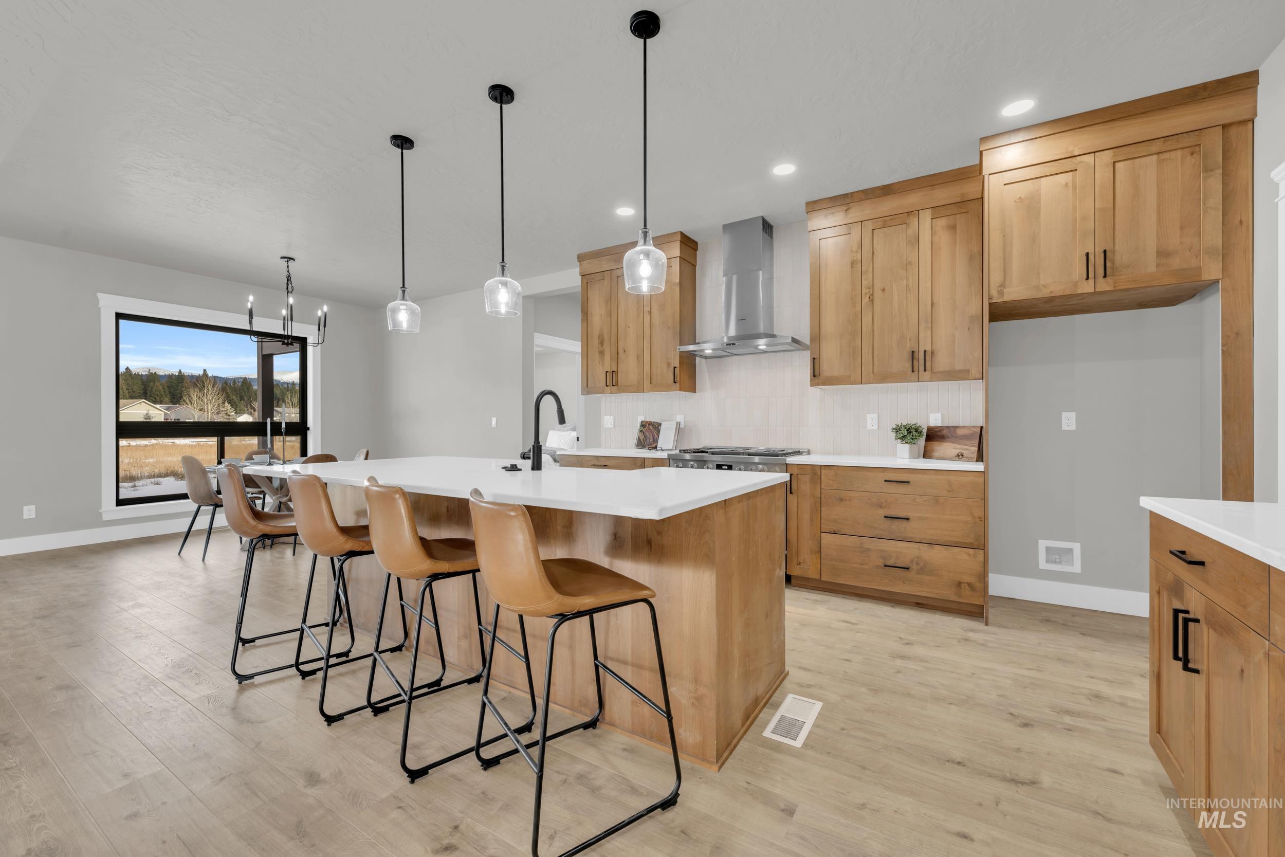 Kitchen featuring backsplash, a breakfast bar area, wall chimney exhaust hood, hanging light fixtures, and an island with sink