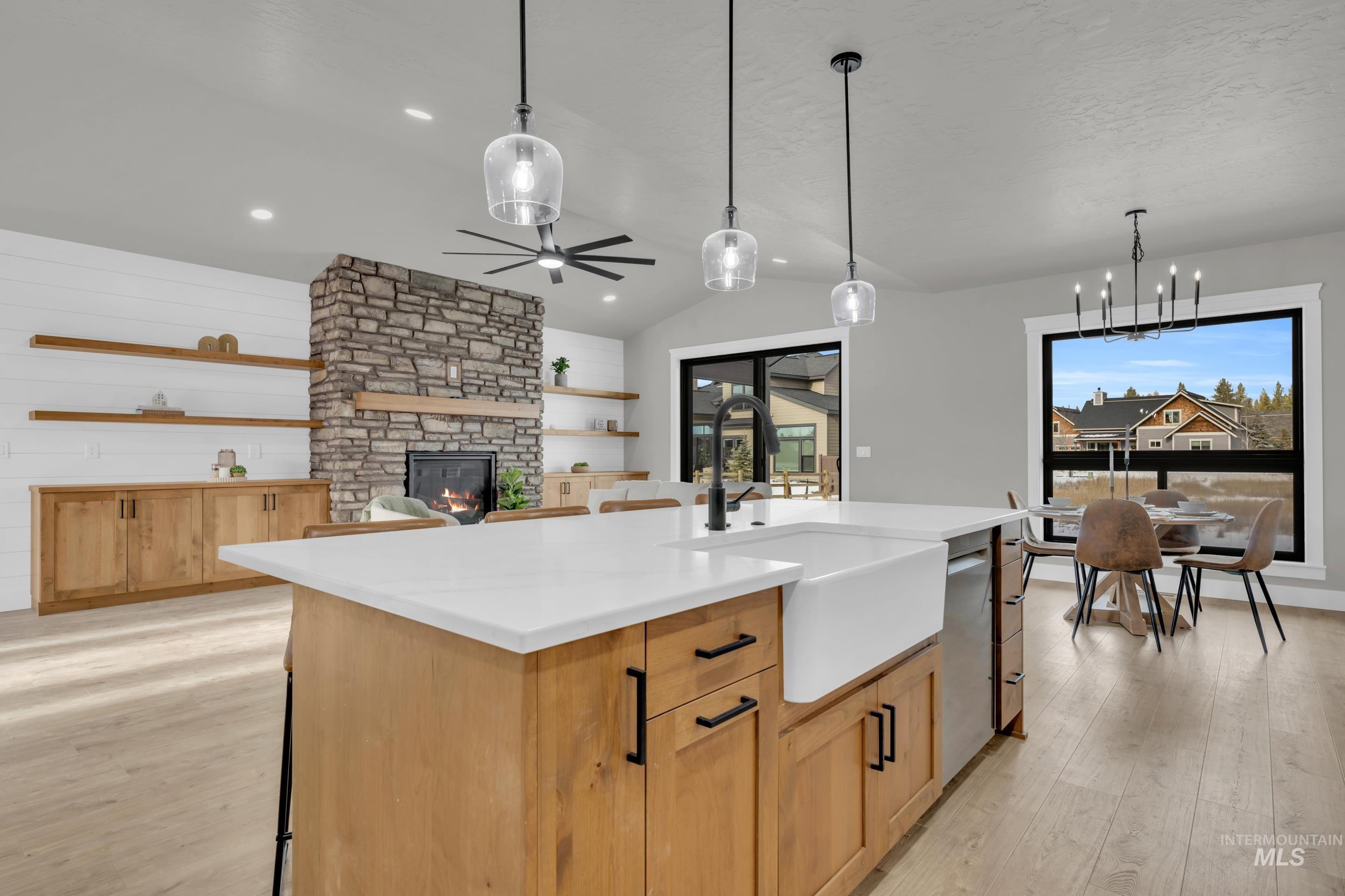 Kitchen featuring a kitchen island with sink, light wood-type flooring, light brown cabinets, a fireplace, and pendant lighting