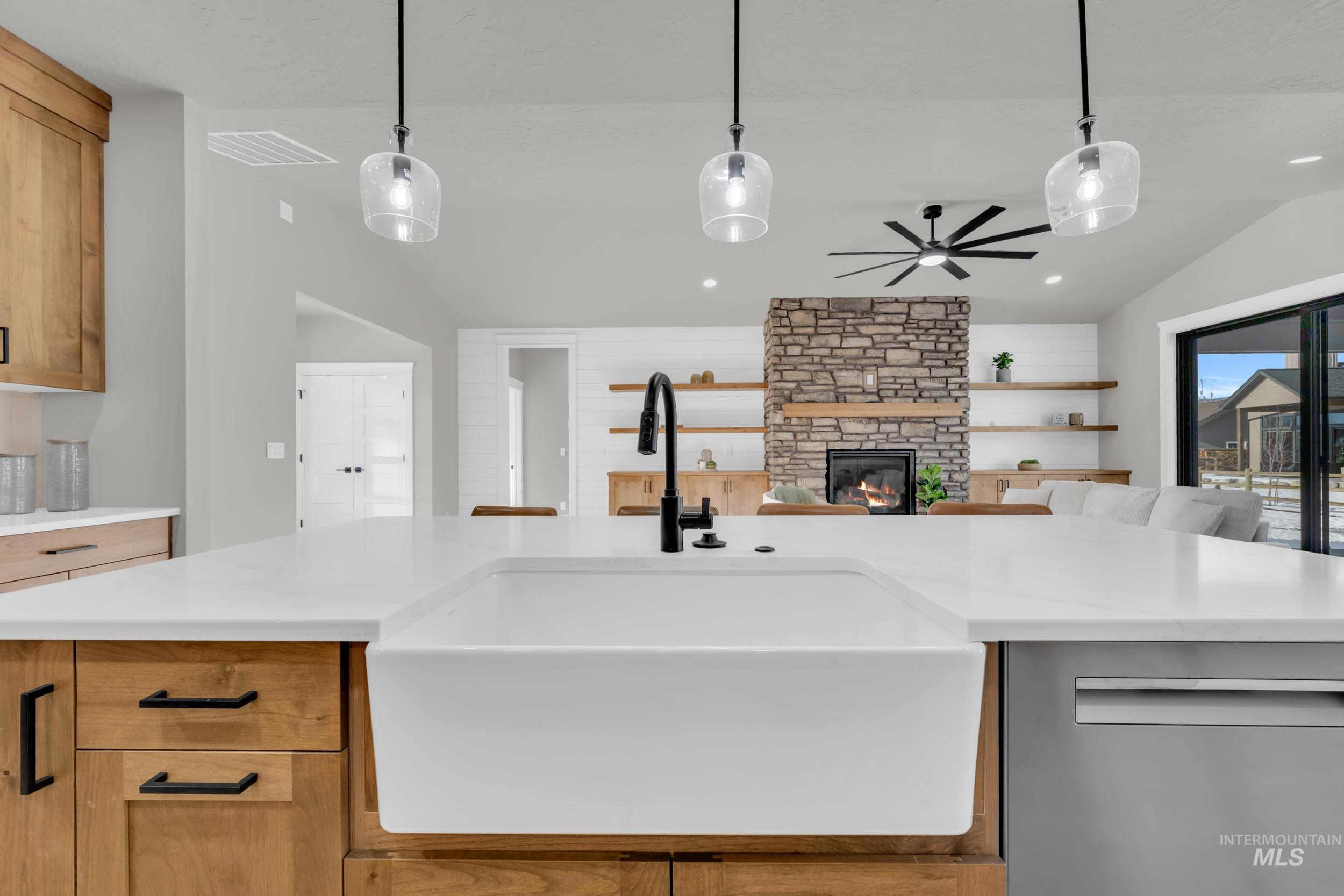 Kitchen with lofted ceiling, dishwasher, pendant lighting, a stone fireplace, and brown cabinetry