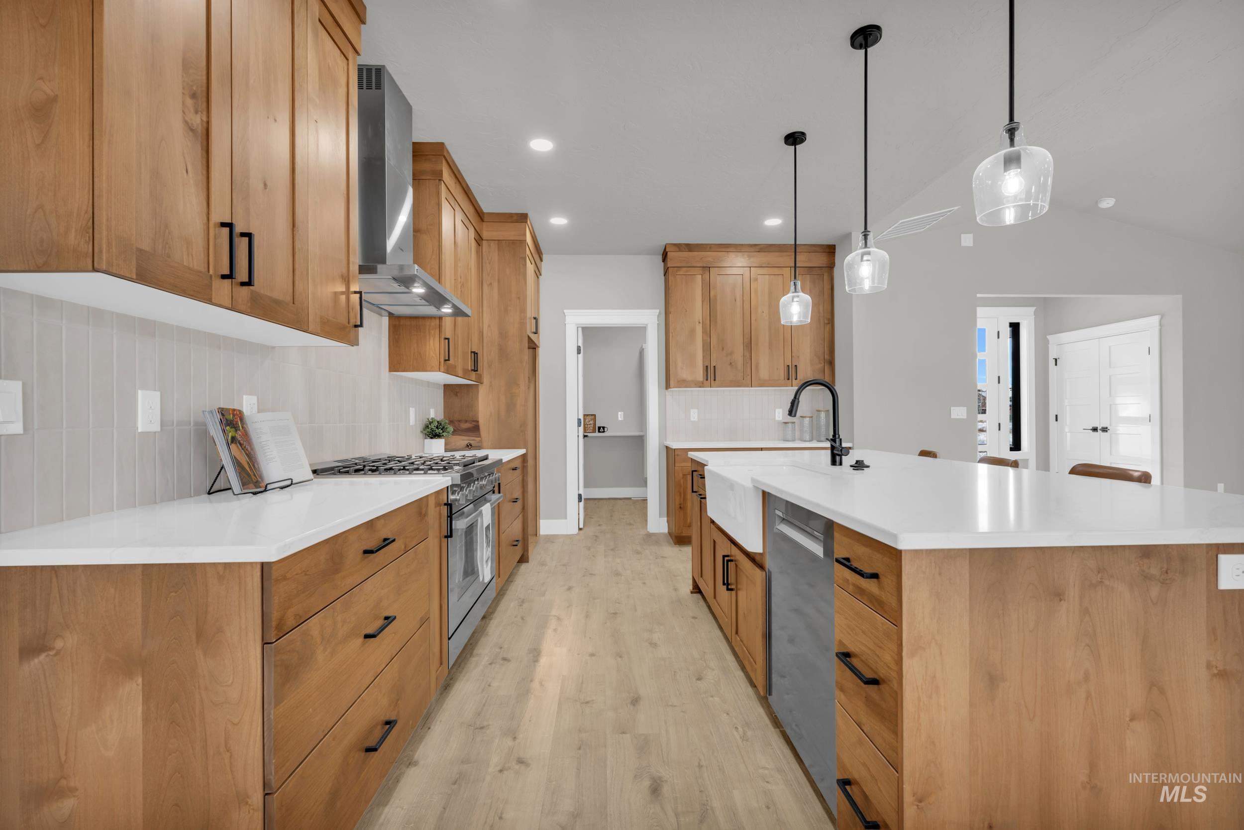 Kitchen featuring a kitchen island with sink, pendant lighting, tasteful backsplash, appliances with stainless steel finishes, and wall chimney exhaust hood