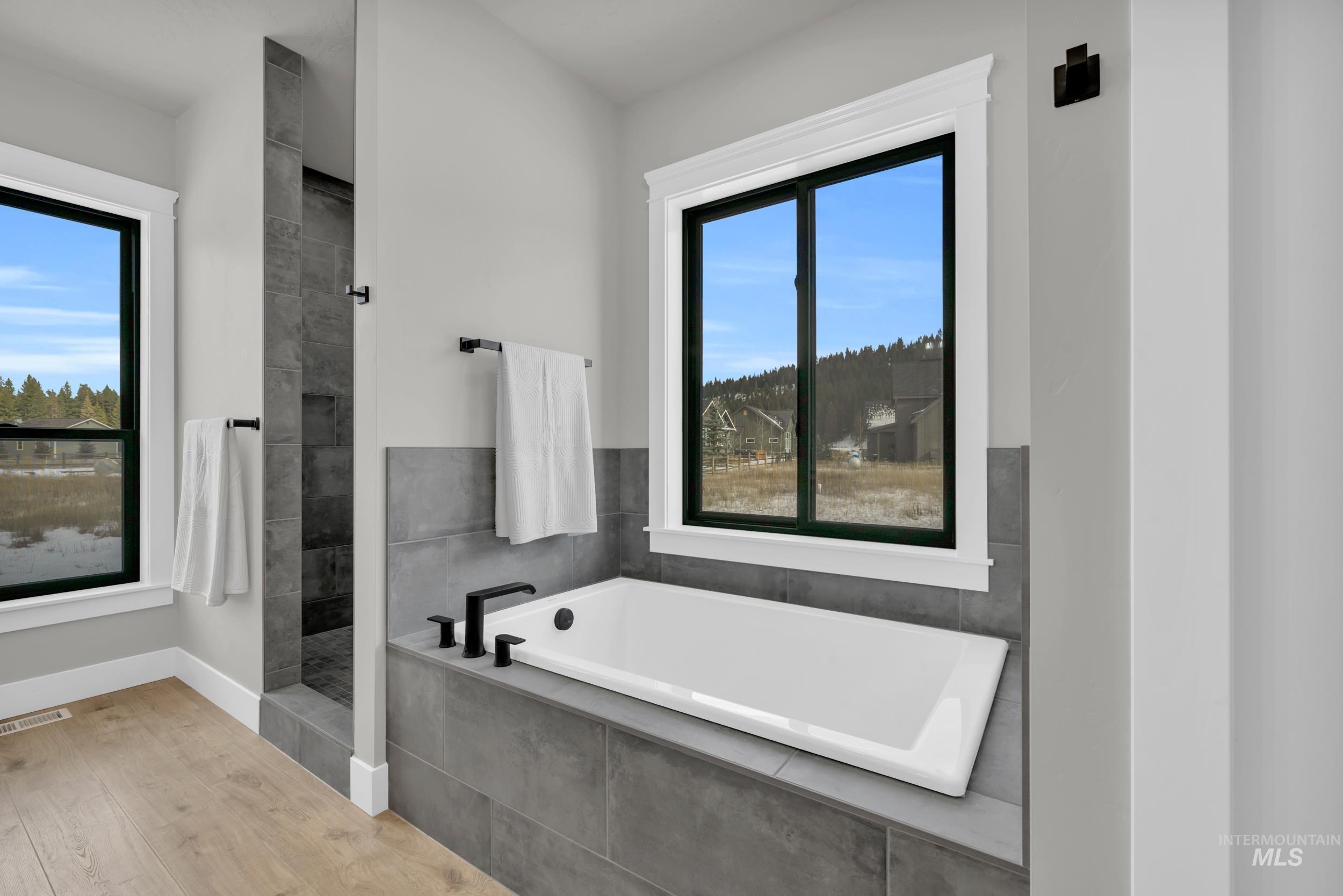 Full bath featuring a garden tub, healthy amount of natural light, a walk in shower, and wood finished floors