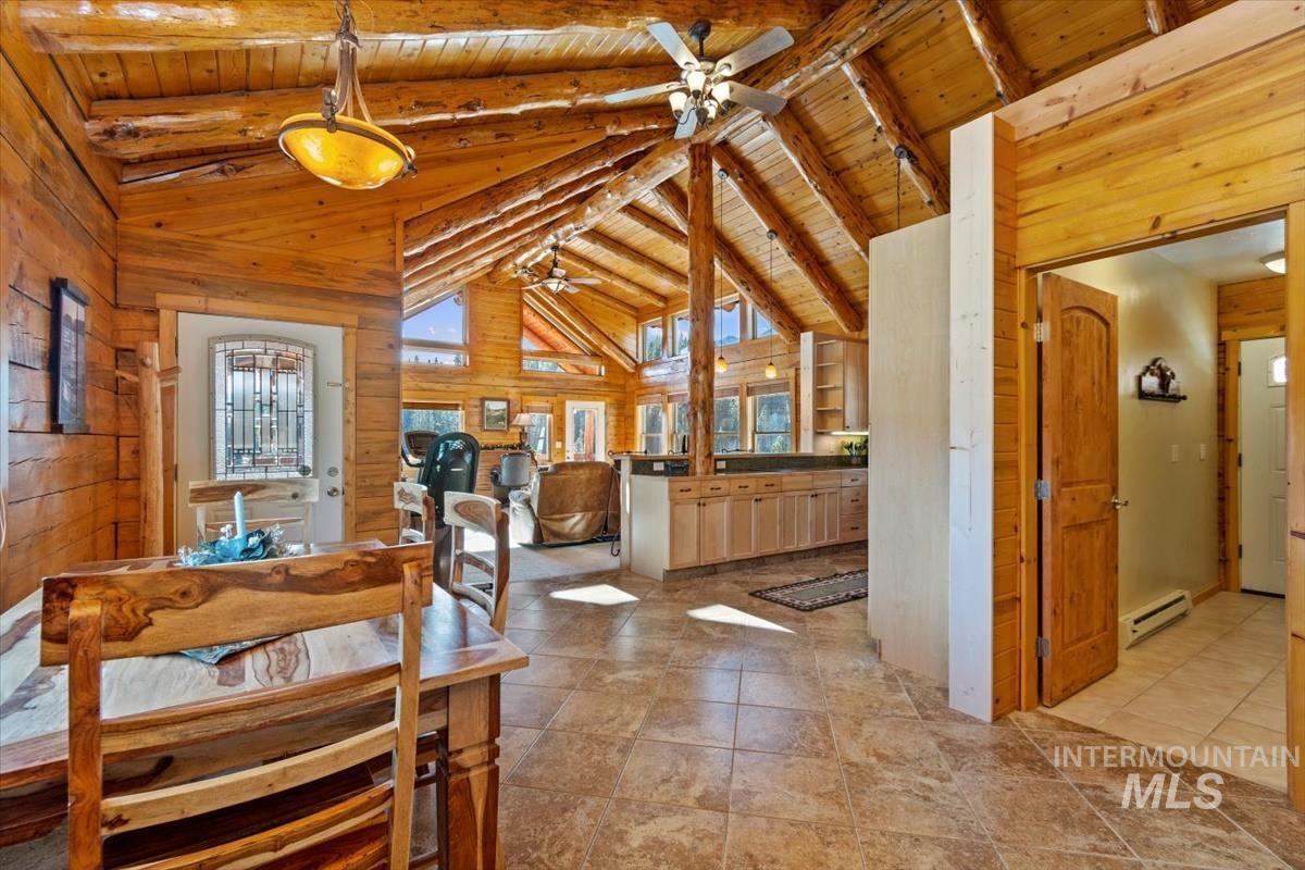 Dining room with wood walls, a wood ceiling with exposed beams, ceiling fan, high vaulted ceiling, and baseboard heating