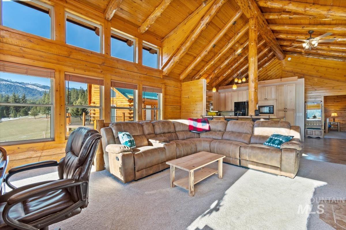 Carpeted living area featuring wood walls, high vaulted ceiling, a wooden ceiling with exposed beams, a mountain view, and ceiling fan
