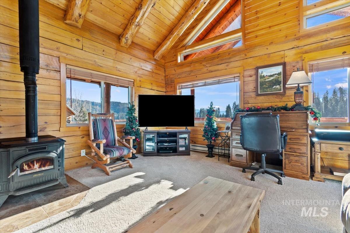 Carpeted living room with a wood stove, wood walls, a wooden ceiling with exposed beams, a baseboard radiator, and high vaulted ceiling