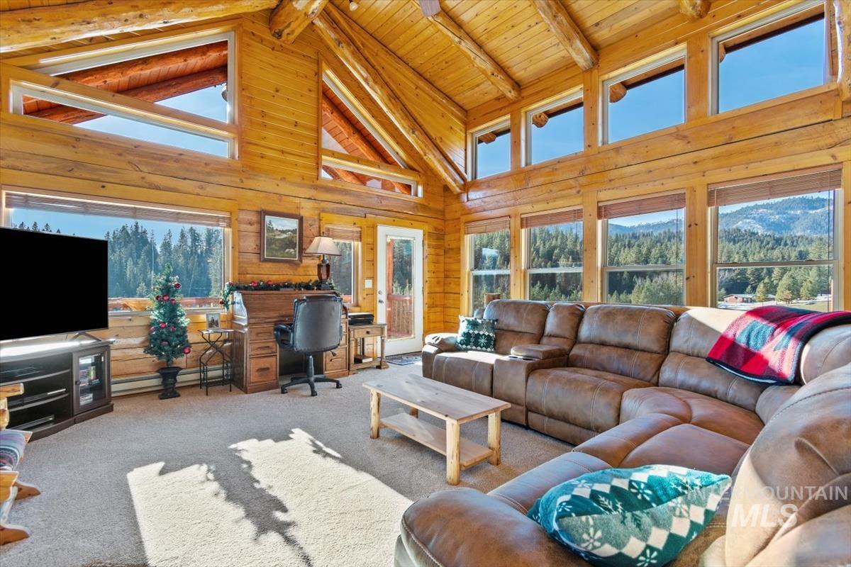 Carpeted living room featuring high vaulted ceiling, wooden walls, a desk, healthy amount of natural light, and a wooden ceiling with exposed beams