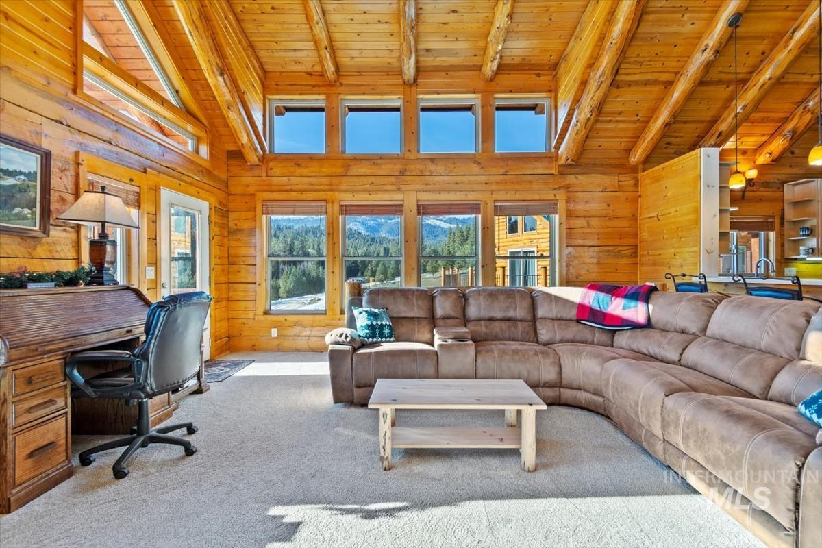 Carpeted living room featuring a wood ceiling with exposed beams, high vaulted ceiling, a desk, and wooden walls