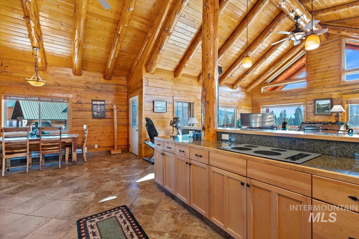 Kitchen featuring wood walls, decorative light fixtures, ceiling fan, light brown cabinetry, and a wooden ceiling with exposed beams