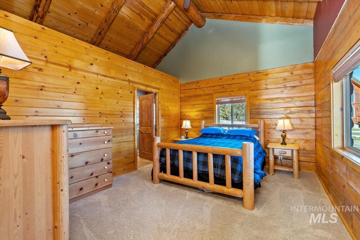 Bedroom with wooden walls, a wood ceiling with exposed beams, high vaulted ceiling, and carpet floors