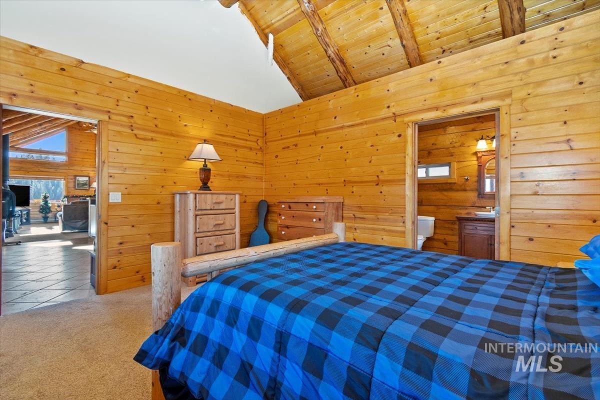 Bedroom with a wooden ceiling with exposed beams, wood walls, carpet floors, and high vaulted ceiling