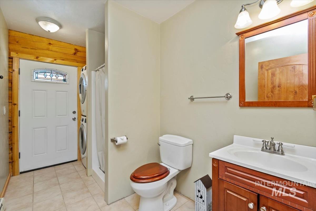Bathroom featuring a stall shower, stacked washing machine and dryer, vanity, and light tile patterned flooring