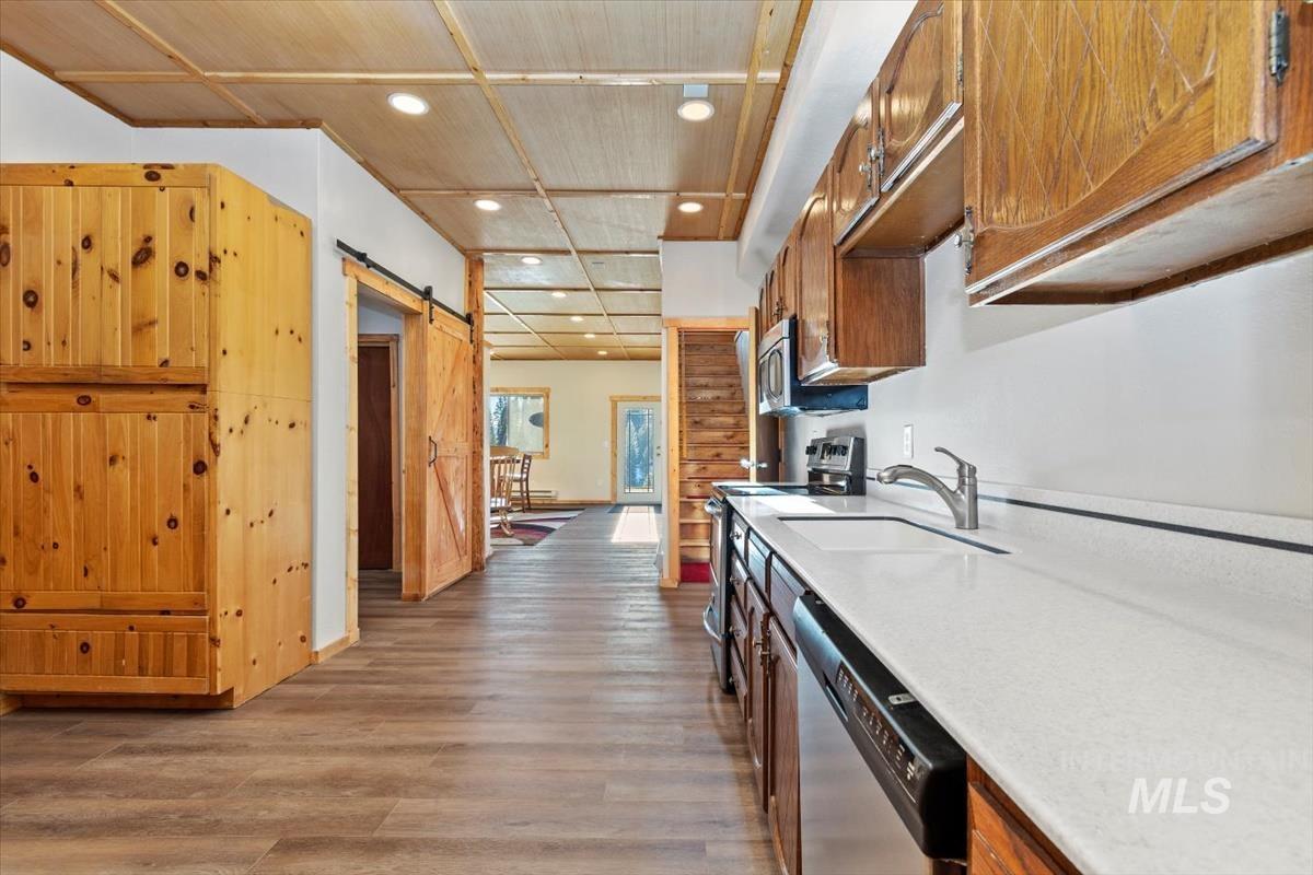 Kitchen with appliances with stainless steel finishes, dark wood-style floors, light stone countertops, a barn door, and recessed lighting