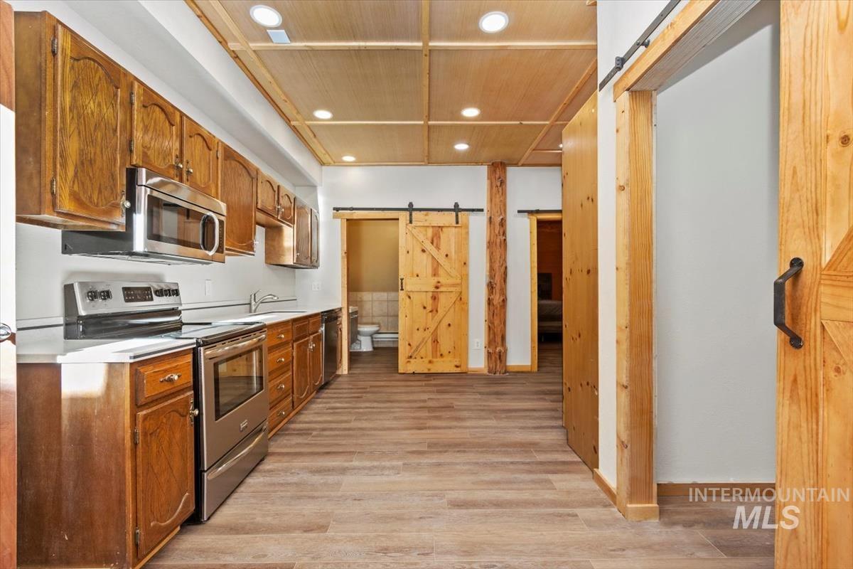 Kitchen featuring a barn door, stainless steel appliances, light countertops, light wood finished floors, and recessed lighting