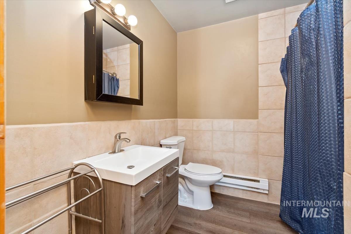 Bathroom with tile walls, vanity, a shower with shower curtain, a wainscoted wall, and a baseboard heating unit