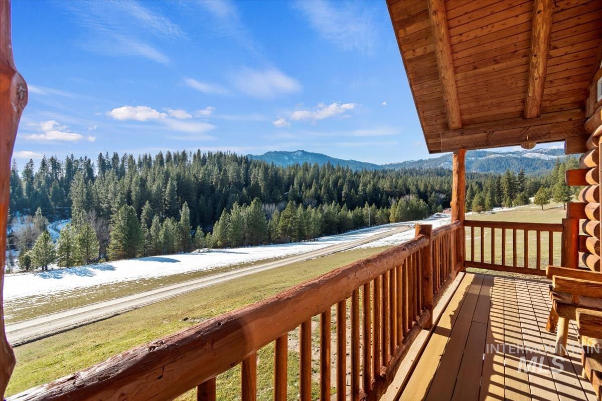 Snow covered deck featuring a forest view, a mountain view, and a lawn