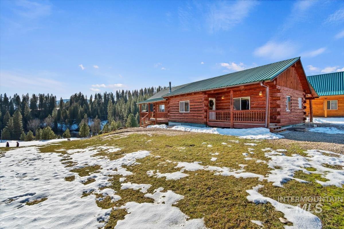 View of snow covered exterior with log siding, covered porch, and a metal roof