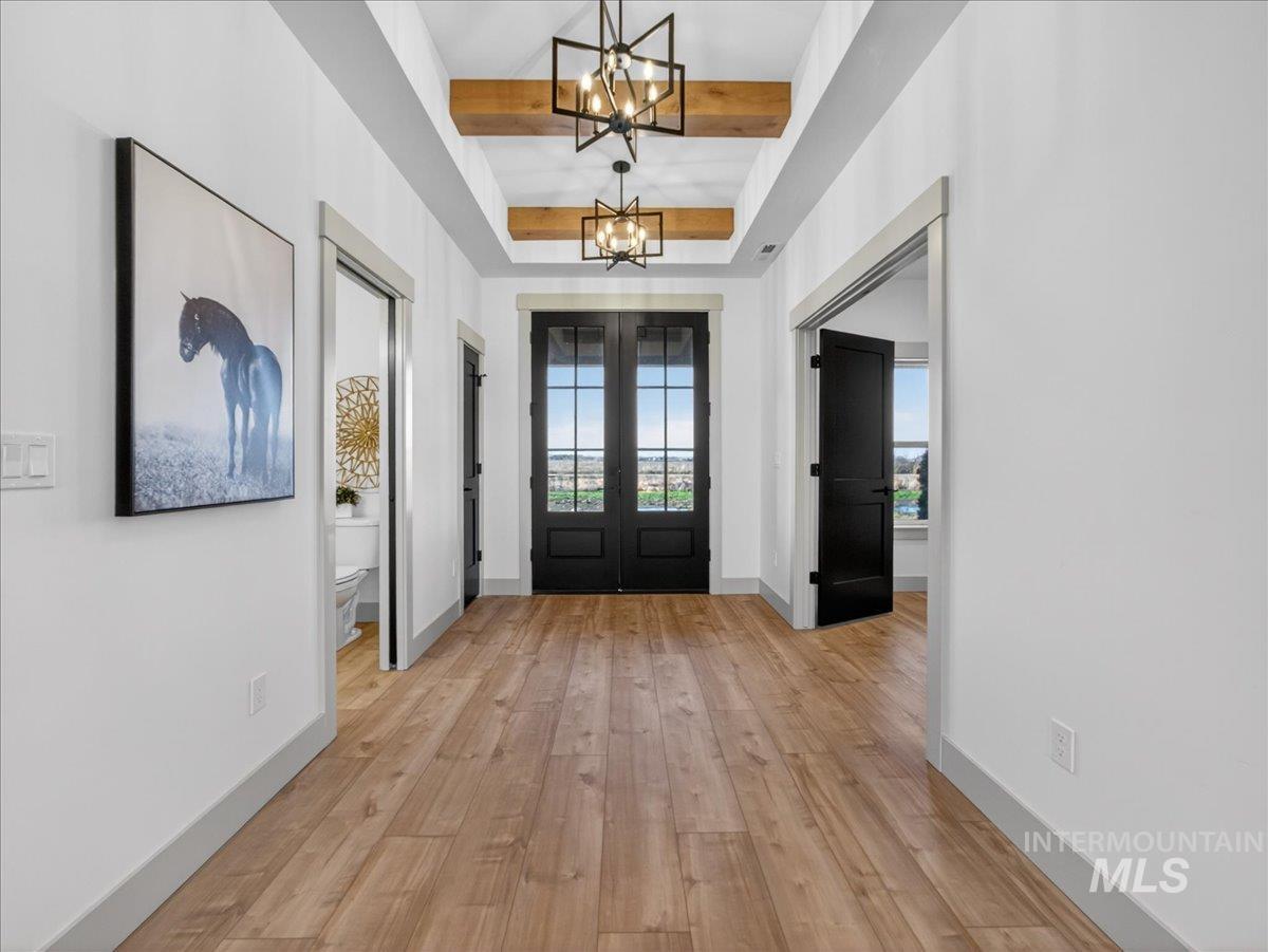 Foyer entrance with beam ceiling, light wood-style floors, french doors, and a chandelier