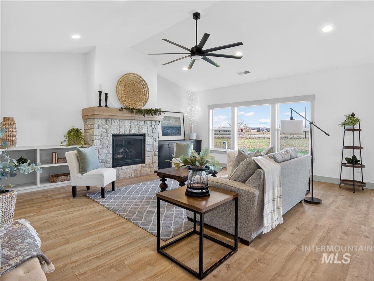 Living area with a stone fireplace, lofted ceiling, light wood-style flooring, a ceiling fan, and recessed lighting
