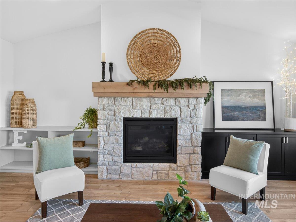 Living room with vaulted ceiling, a stone fireplace, and wood finished floors