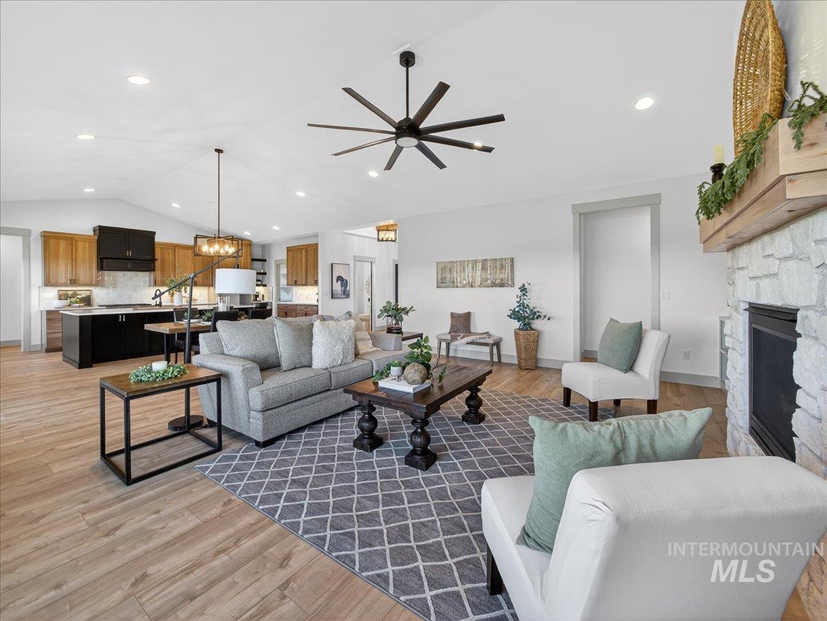 Living area with vaulted ceiling, a chandelier, ceiling fan, light wood-type flooring, and a fireplace
