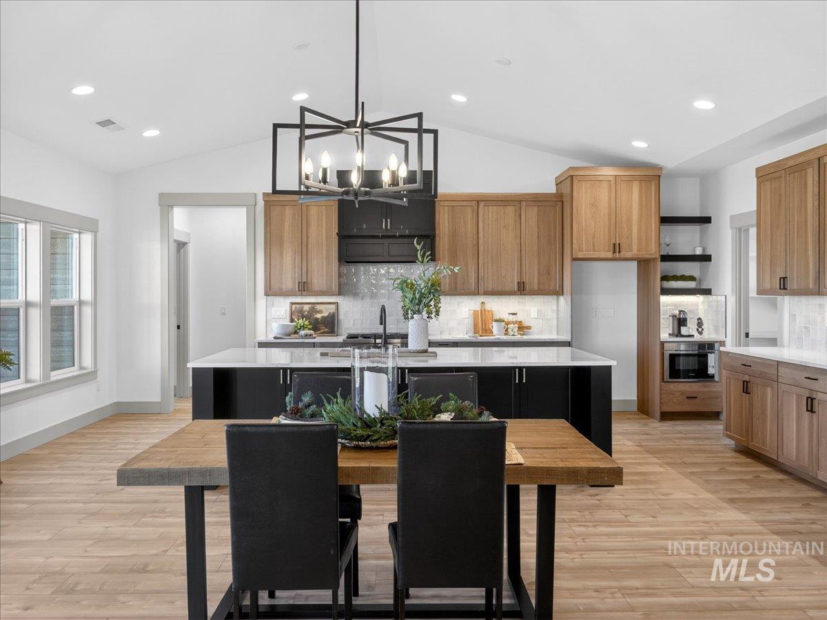 Kitchen featuring brown cabinetry, vaulted ceiling, open shelves, an island with sink, and recessed lighting