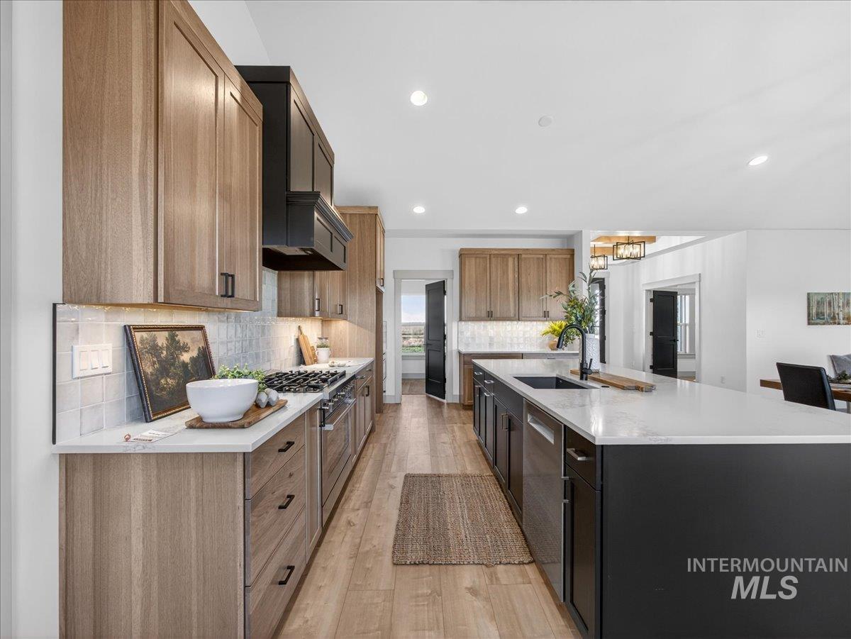 Kitchen with a spacious island, light wood-type flooring, light stone counters, recessed lighting, and stainless steel appliances