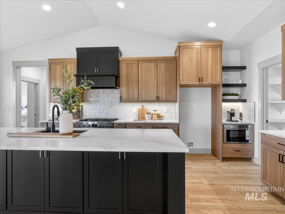 Kitchen featuring open shelves, light stone countertops, light wood finished floors, tasteful backsplash, and lofted ceiling