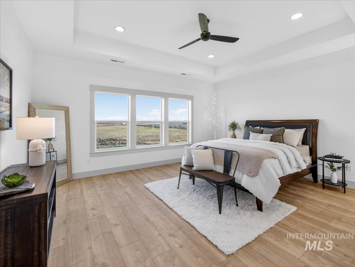 Bedroom with a tray ceiling, light wood finished floors, ceiling fan, and recessed lighting