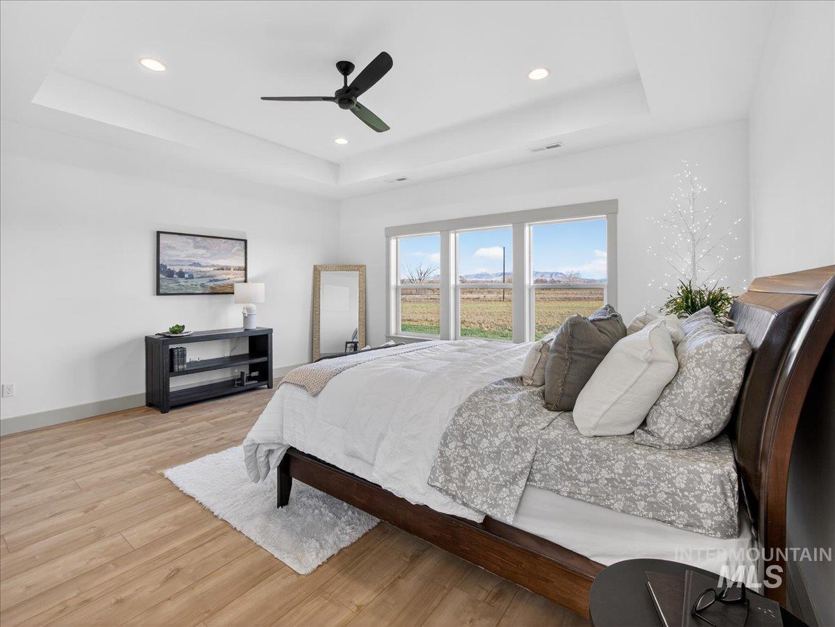 Bedroom with light wood-style flooring, a tray ceiling, ceiling fan, and recessed lighting