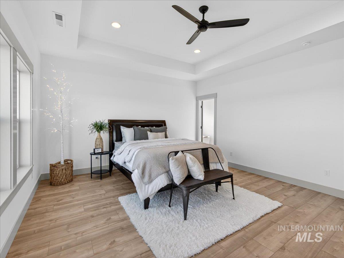 Bedroom featuring a tray ceiling, light wood-style flooring, ceiling fan, and recessed lighting