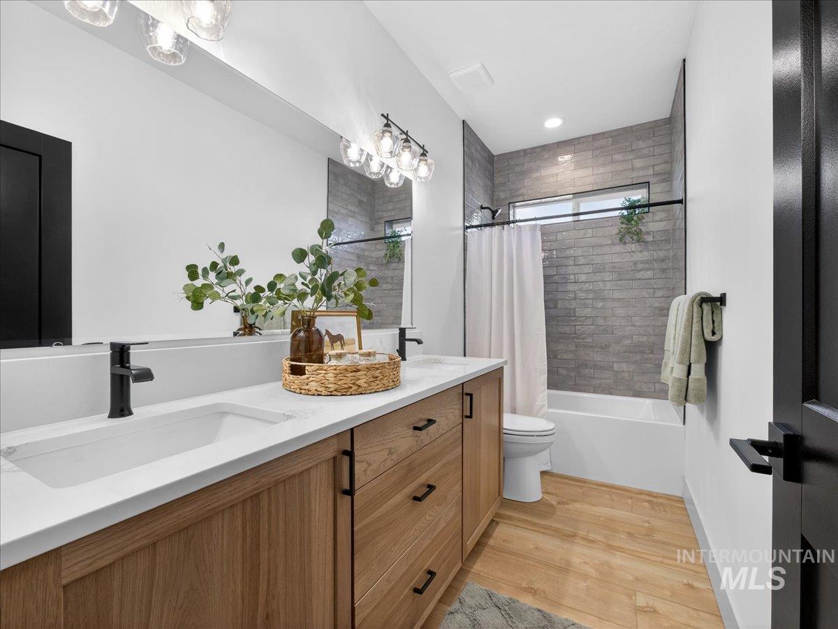 Bathroom with double vanity, shower / tub combo, and light wood-style floors
