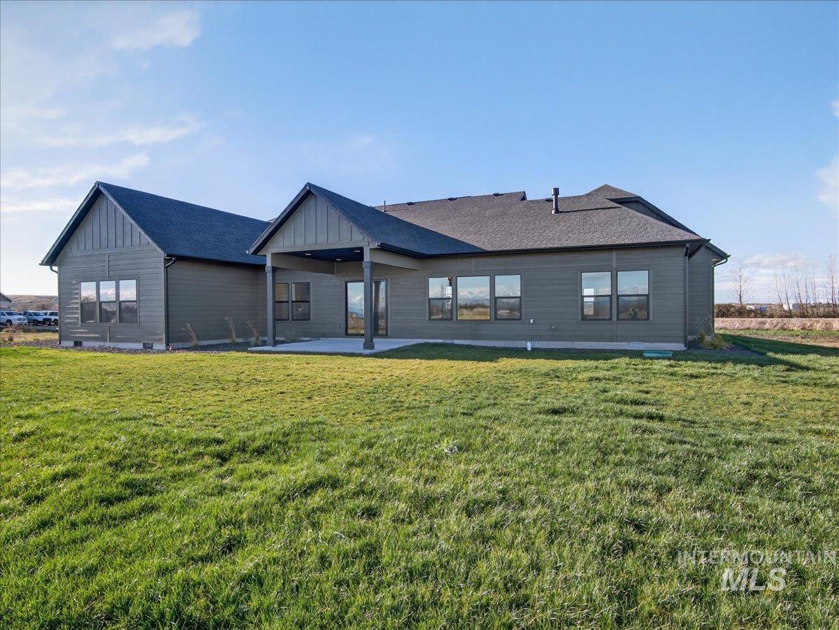 Back of house with board and batten siding, a yard, a patio, and roof with shingles