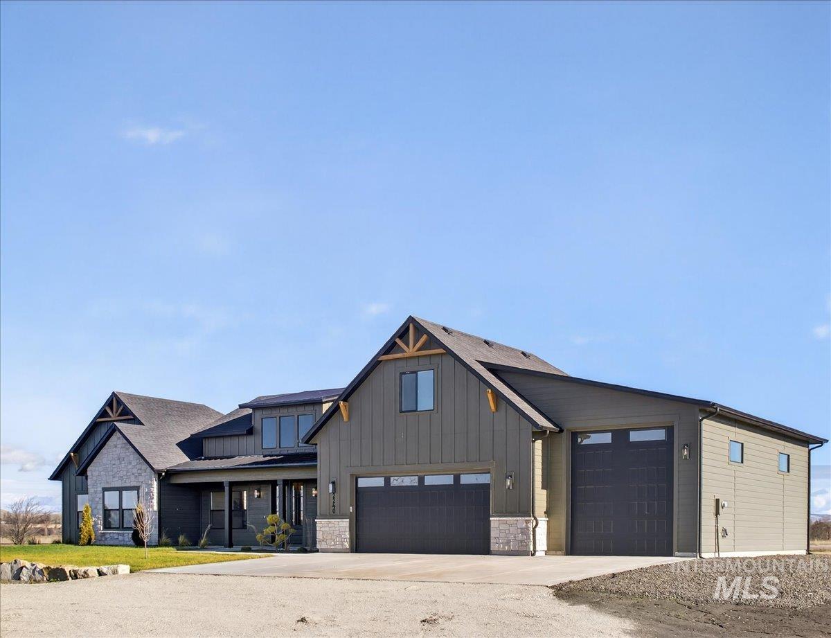 Modern farmhouse style home featuring stone siding, a garage, driveway, and board and batten siding