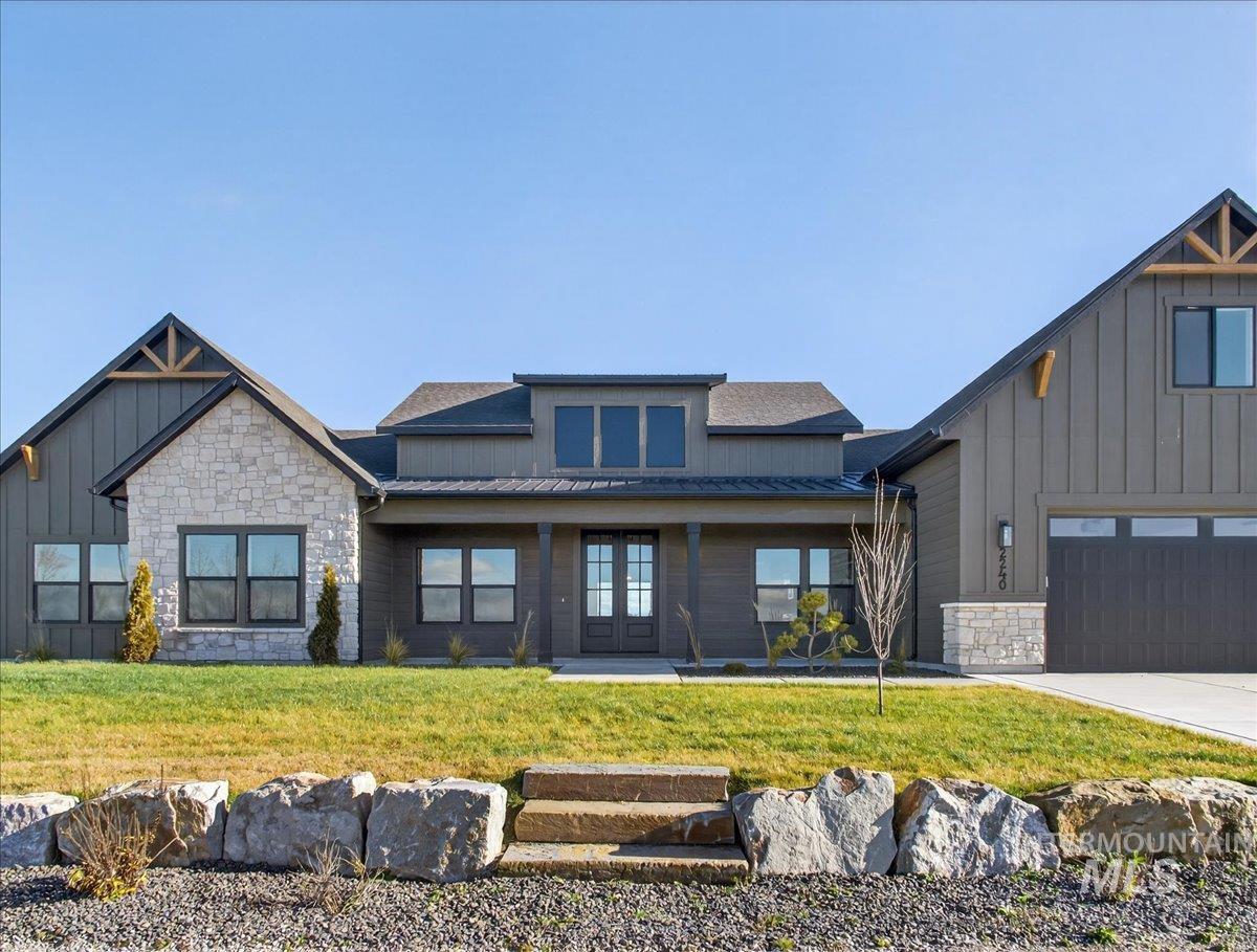 View of front of property with stone siding, board and batten siding, covered porch, a front yard, and concrete driveway