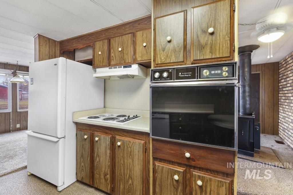 Kitchen featuring wooden walls, carpet flooring, white appliances, brown cabinetry, and light countertops