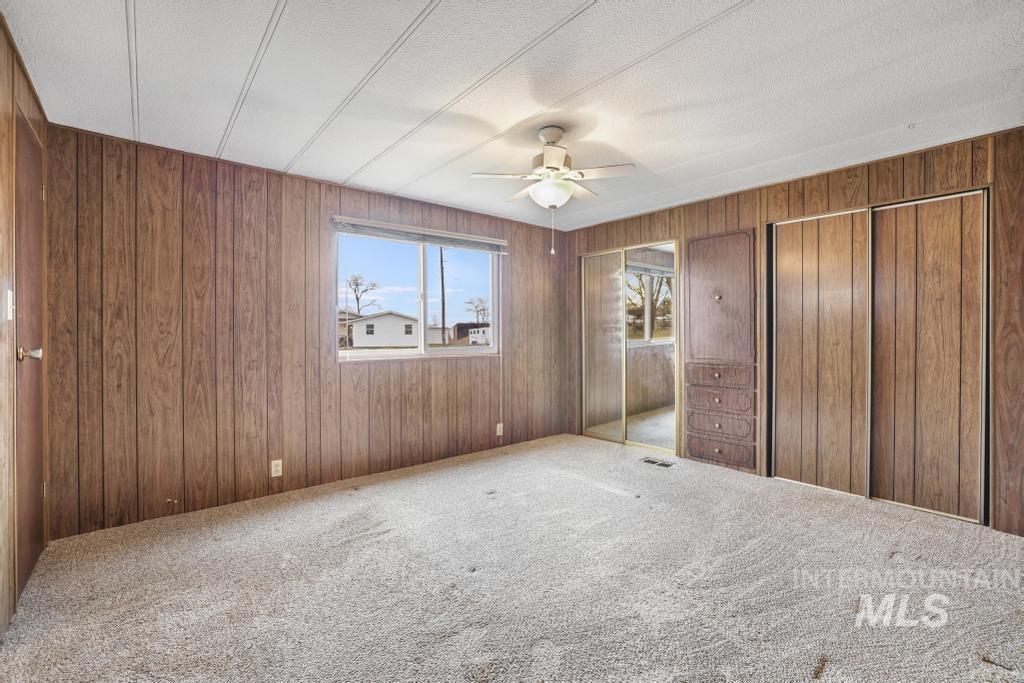 Unfurnished bedroom featuring wood walls, multiple closets, carpet floors, ceiling fan, and a textured ceiling