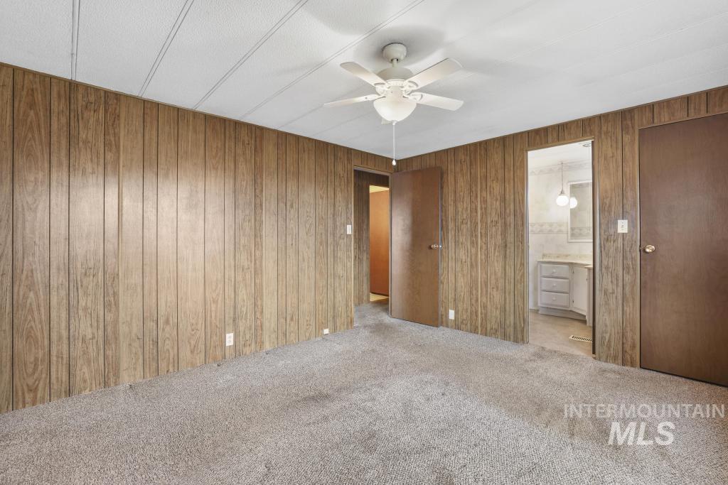 Unfurnished bedroom featuring wooden walls, carpet flooring, connected bathroom, and a ceiling fan