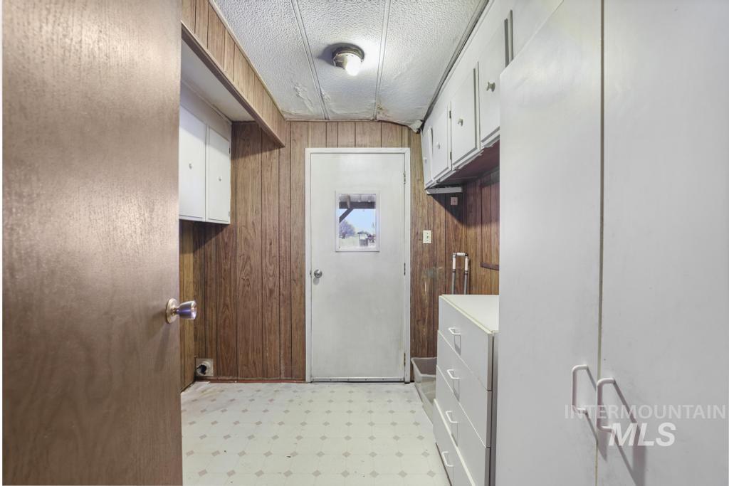 Laundry room with light floors, wooden walls, a textured ceiling, and cabinet space