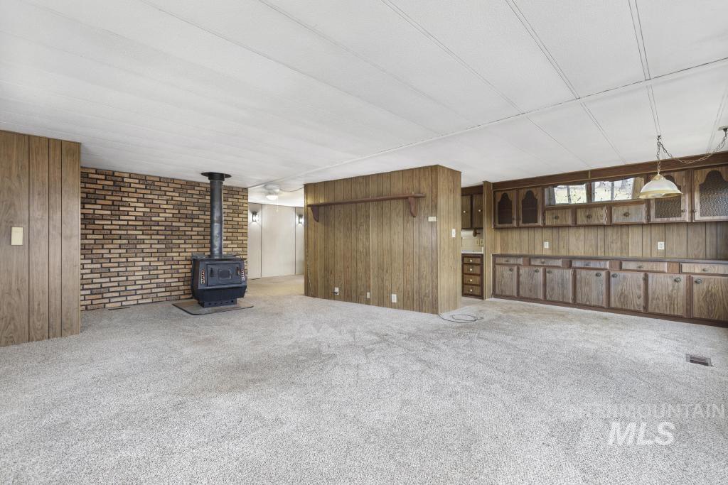 Unfurnished living room with wood walls, a wood stove, and carpet flooring