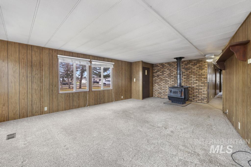 Unfurnished living room with a wood stove, wooden walls, and carpet flooring
