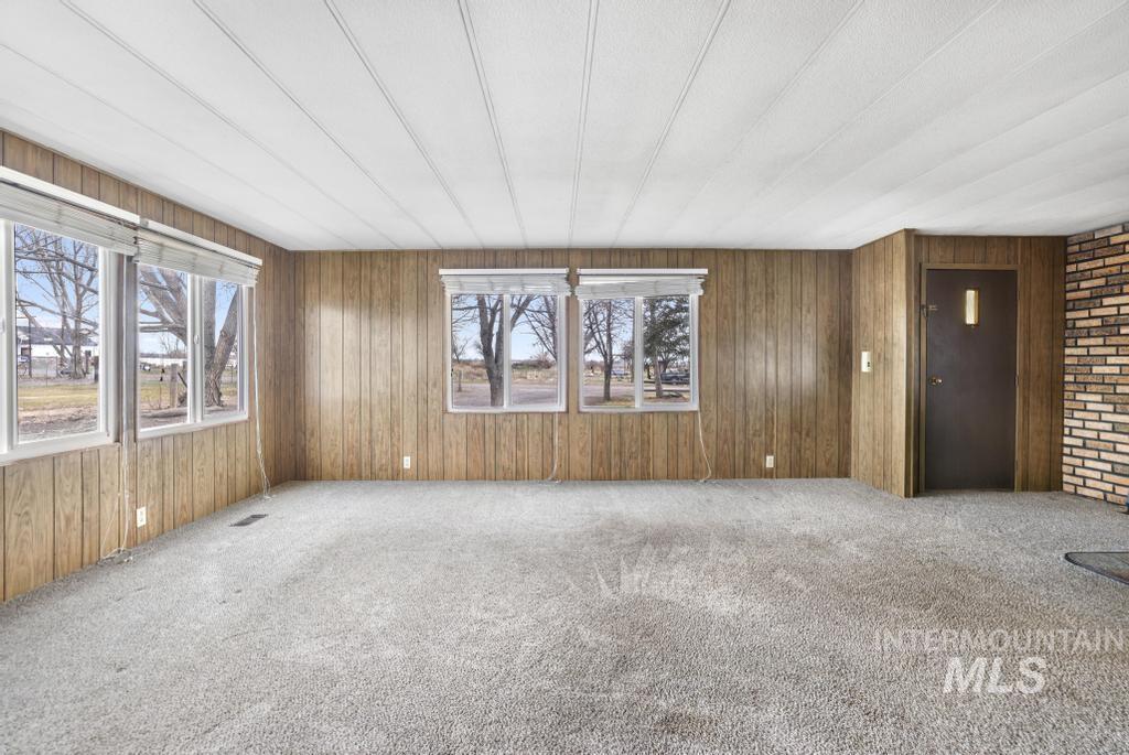 Empty room featuring carpet floors, healthy amount of natural light, and wood walls