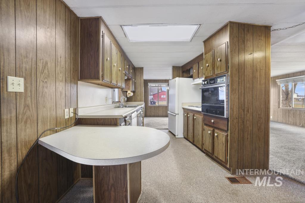 Kitchen with wooden walls, light colored carpet, light countertops, black oven, and freestanding refrigerator