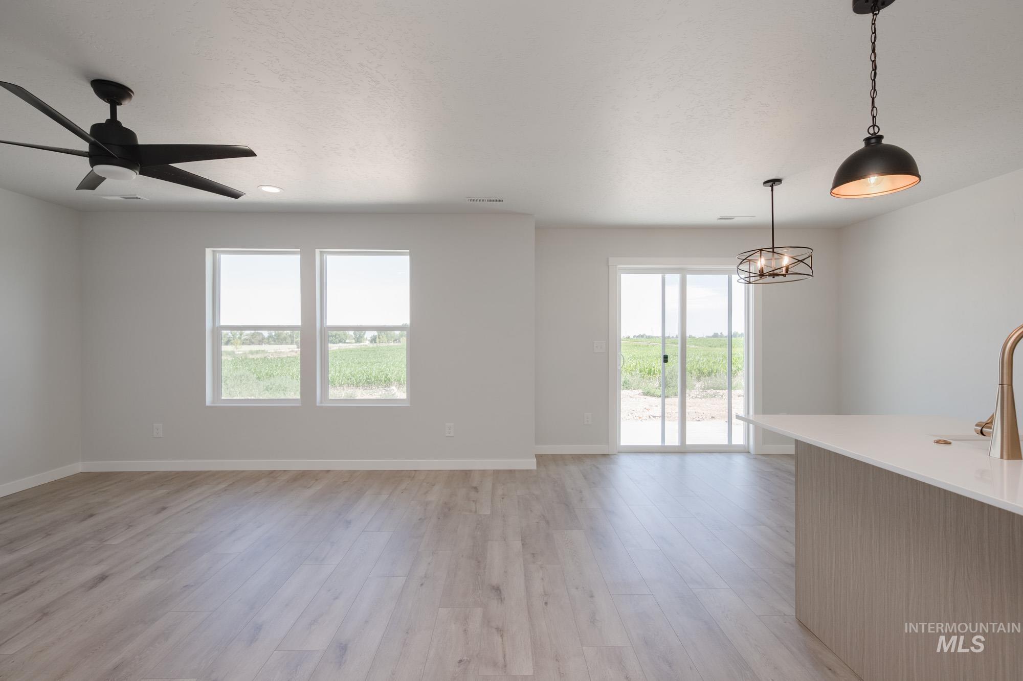 Unfurnished living room with healthy amount of natural light, light wood finished floors, a chandelier, a ceiling fan, and recessed lighting